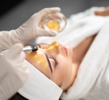Beautician in sterile gloves applying cosmetic mask on woman face