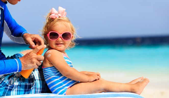 father applying sunblock cream on daughters shoulder, sun protection